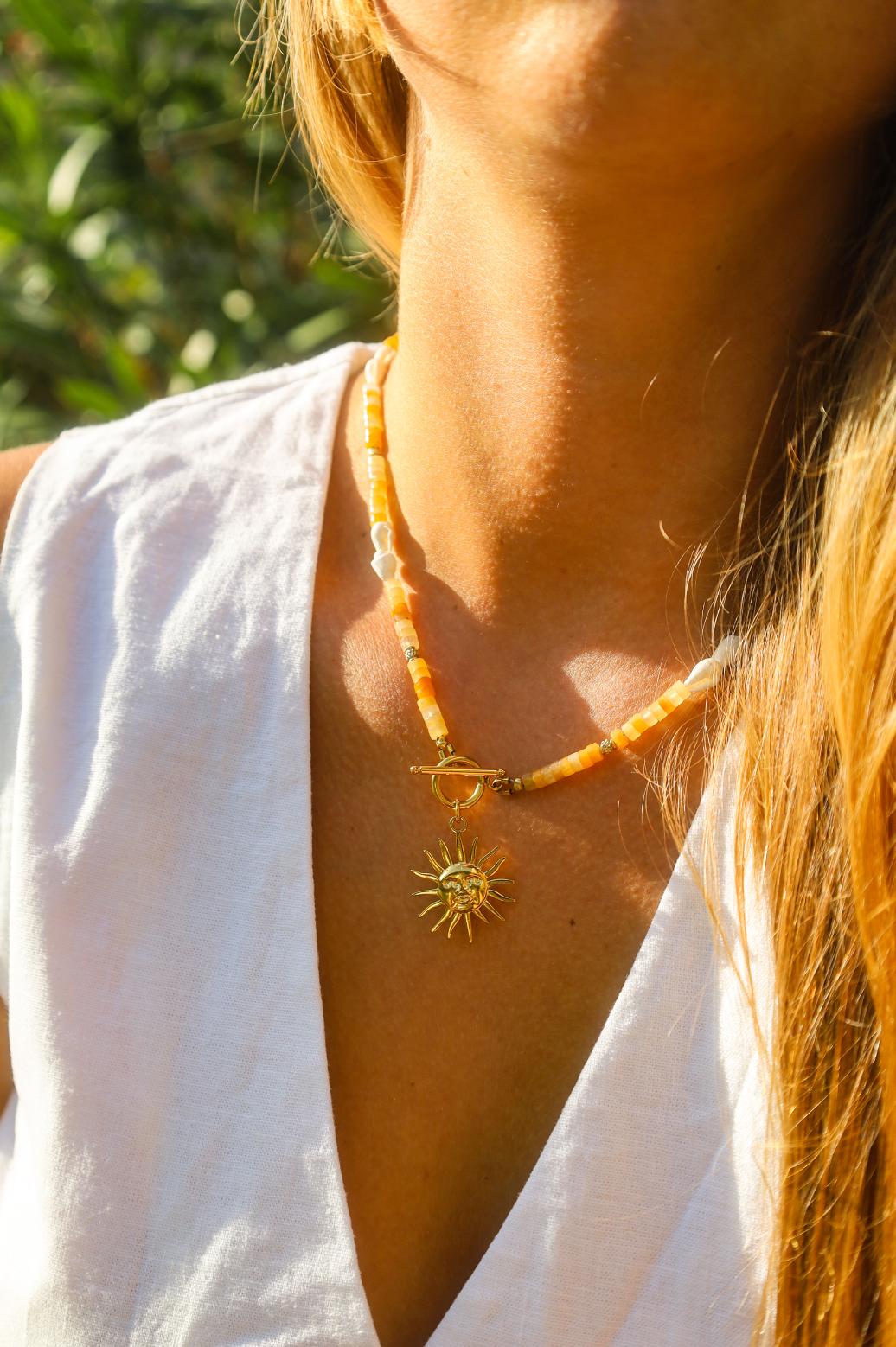 Collier en jade jaune naturelles avec des petits coquillages blancs et des touches dorées avec une ouverture à l'avant et à l'arrière et un pendentif soleil.
