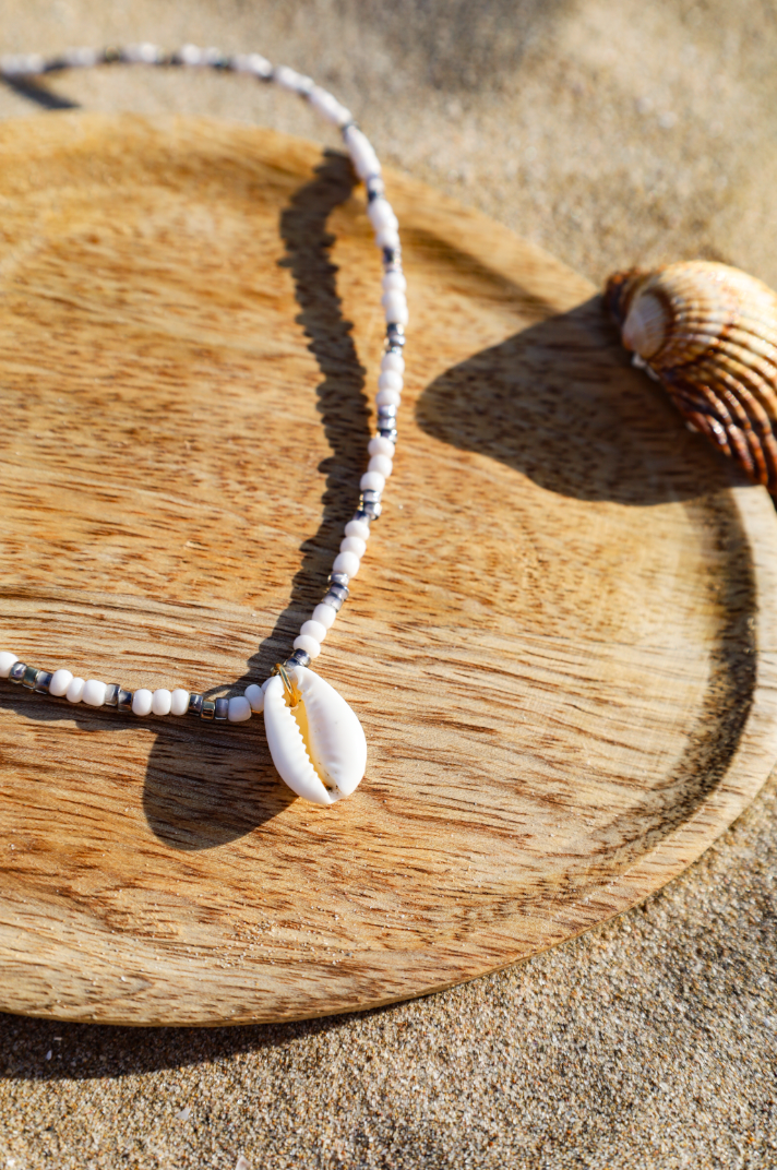 Collier composé de perles de petites rocailles couleur violet et blanc avec pendentif cauri
